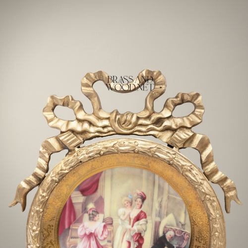 طبق بورسلان مستدير بإطار نحاسي نيوكلاسيكي مُتوَّج بفيونكة منحوتة ومشهد صالون مرسوم يدوياً